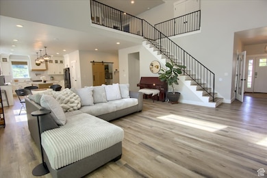 Living area with a barn door, a chandelier, stairway, light wood-style flooring, and a towering ceiling