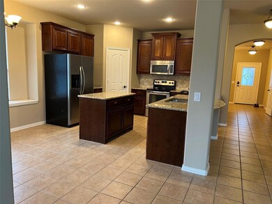 Kitchen with light stone countertops, stainless steel appliances, light tile floors, a kitchen island, and tasteful backsplash