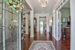 Foyer with dark wood-type flooring, ornate columns, a notable chandelier, and ornamental molding