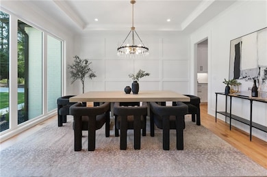 Dining room featuring a decorative wall, healthy amount of natural light, light wood-type flooring, a raised ceiling, and crown molding
