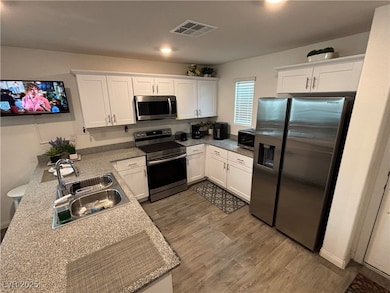 Kitchen featuring white cabinetry, stainless steel appliances, dark wood-style floors, a peninsula, and light stone counters
