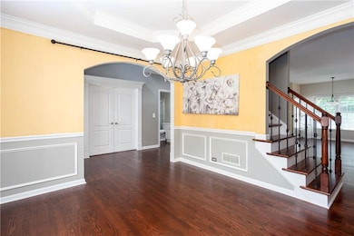 Unfurnished dining area featuring arched walkways, a chandelier, wood finished floors, wainscoting, and ornamental molding