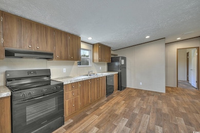 Kitchen with dark wood-type flooring, under cabinet range hood, a sink, black appliances, and brown cabinetry
