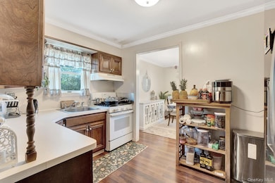 Kitchen featuring white range with gas cooktop, light countertops, brown cabinets, and dark wood finished floors