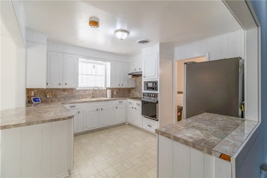 Kitchen featuring a peninsula, white cabinetry, tasteful backsplash, black appliances, and wood counters