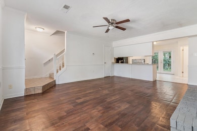 Unfurnished living room featuring wood finished floors, ornamental molding, a textured ceiling, a ceiling fan, and stairs