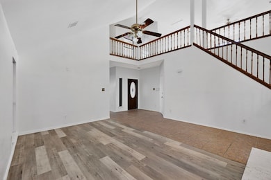 Unfurnished living room featuring high vaulted ceiling, light wood finished floors, a ceiling fan, and stairway