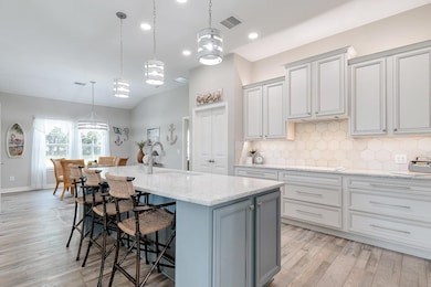 Kitchen with decorative light fixtures, light stone counters, gray cabinets, a breakfast bar, and decorative backsplash