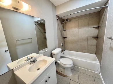 Full bathroom featuring vanity, tiled shower / bath combo, a textured ceiling, tile patterned floors, and toilet
