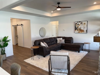 Living room featuring a barn door, dark wood-type flooring, a tray ceiling, ceiling fan, and recessed lighting