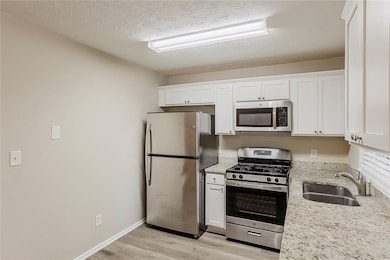Kitchen with stainless steel appliances, a sink, light wood-style floors, white cabinetry, and a textured ceiling