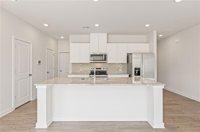 Kitchen featuring appliances with stainless steel finishes, an island with sink, light wood finished floors, backsplash, and white cabinetry