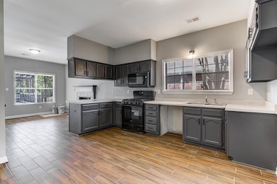 Kitchen featuring black appliances, wood finished floors, and light countertops