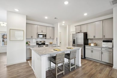 Kitchen featuring light stone countertops, appliances with stainless steel finishes, hardwood / wood-style flooring, tasteful backsplash, and a center island with sink
