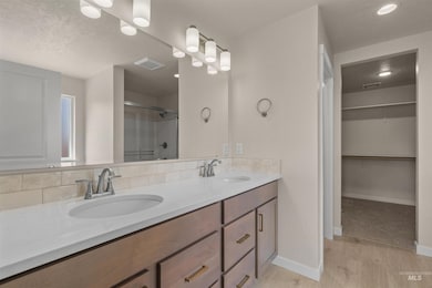 Full bath with a stall shower, a textured ceiling, light wood finished floors, a spacious closet, and double vanity