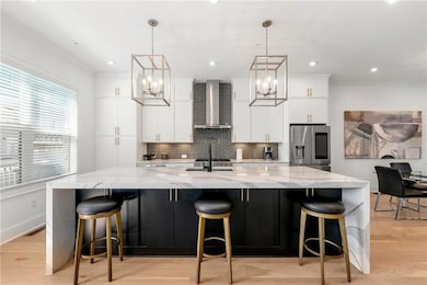 Kitchen featuring stainless steel fridge with ice dispenser, wall chimney range hood, a spacious island, decorative backsplash, and a chandelier