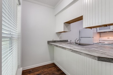 Kitchen with ornamental molding, dark wood-type flooring, light countertops, white appliances, and white cabinets