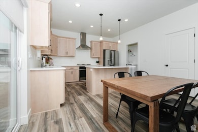 Kitchen featuring light brown cabinetry, a kitchen island, light wood-style flooring, appliances with stainless steel finishes, and wall chimney exhaust hood