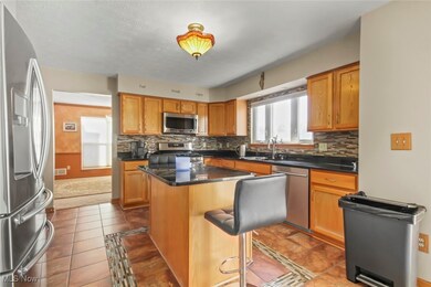Kitchen featuring appliances with stainless steel finishes, light tile patterned floors, a center island, tasteful backsplash, and brown cabinetry