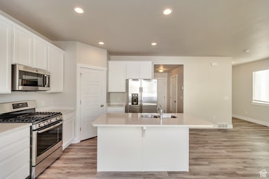 Kitchen with appliances with stainless steel finishes, white cabinetry, recessed lighting, an island with sink, and light wood-type flooring