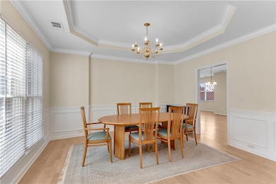 Dining room featuring a chandelier, light wood-type flooring, a raised ceiling, wainscoting, and crown molding
