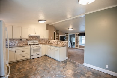 Kitchen featuring white appliances, a peninsula, tasteful backsplash, white cabinets, and dark colored carpet