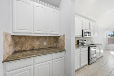 Kitchen with stainless steel appliances, decorative backsplash, white cabinetry, light tile patterned flooring, and dark stone countertops