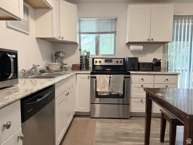 Kitchen featuring stainless steel appliances, white cabinets, light countertops, light wood-style flooring, and a textured wall