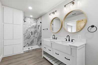 Bathroom with double vanity, a marble finish shower, light wood-type flooring, and recessed lighting