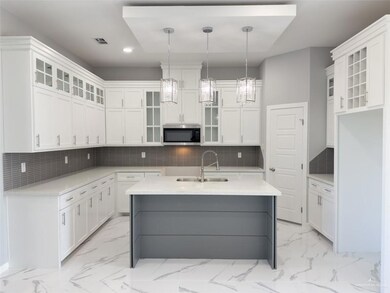Kitchen with hanging light fixtures, white cabinets, and a kitchen island with sink