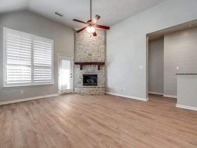 Unfurnished living room featuring a stone fireplace, light wood finished floors, a ceiling fan, and vaulted ceiling