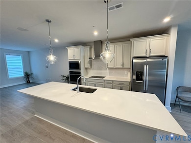 Kitchen featuring stainless steel appliances, hanging light fixtures, light wood-style floors, backsplash, and a center island with sink