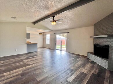 Unfurnished living room featuring dark wood-type flooring, ceiling fan, vaulted ceiling with beams, a textured ceiling, and a brick fireplace