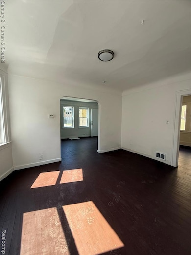 Unfurnished room featuring arched walkways and dark wood-style floors