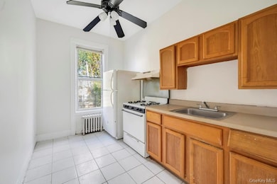 Kitchen with white appliances, light tile patterned floors, light countertops, radiator heating unit, and under cabinet range hood