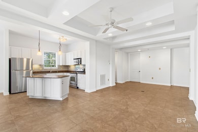 Kitchen with a raised ceiling, appliances with stainless steel finishes, decorative light fixtures, open floor plan, and a center island