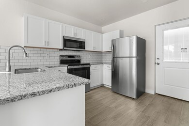 Kitchen with stainless steel appliances, white cabinets, decorative backsplash, and light stone counters