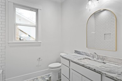 The guest bath is well appointed with a beautiful white shaker vanity, marble countertops, and polished chrome fixtures with a contrasting matte gold framed mirror.