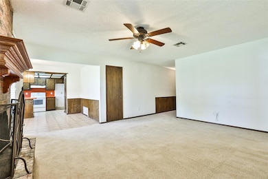 Unfurnished living room with ceiling fan, light carpet, a textured ceiling, and wainscoting