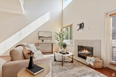 Living room with healthy amount of natural light, a towering ceiling, a fireplace, and wood finished floors