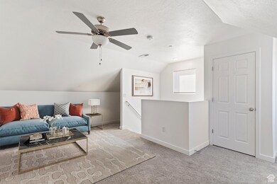 Sitting room featuring an upstairs landing, lofted ceiling, carpet flooring, a textured ceiling, and ceiling fan. Staged