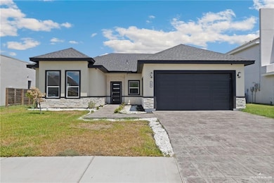 Prairie-style house with a front lawn, stone siding, a shingled roof, stucco siding, and decorative driveway