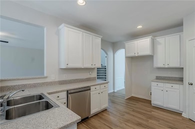 Kitchen with stainless steel dishwasher, a sink, arched walkways, white cabinetry, and recessed lighting