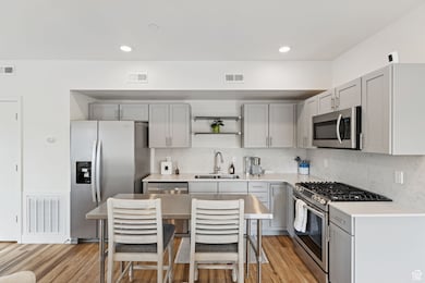 Kitchen featuring gray cabinetry, stainless steel appliances, light wood-style flooring, decorative backsplash, and open shelves
