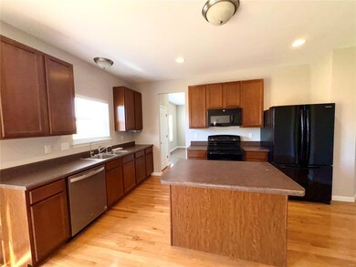 Kitchen with a sink, black appliances, a kitchen island, and light wood-style flooring