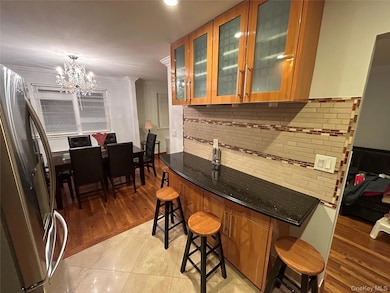 Bar with freestanding refrigerator, dark stone counters, decorative backsplash, brown cabinetry, and ornamental molding