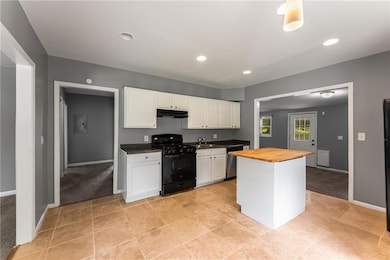 Kitchen featuring black range with gas stovetop, under cabinet range hood, butcher block countertops, dishwasher, and white cabinetry