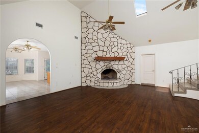 Unfurnished living room featuring ceiling fan, high vaulted ceiling, wood finished floors, a stone fireplace, and arched walkways
