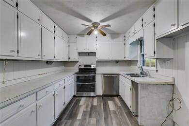 Kitchen featuring stainless steel appliances, white cabinets, light countertops, a textured ceiling, and dark wood finished floors