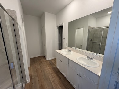Full bath with double vanity, dark wood-style flooring, and a shower stall